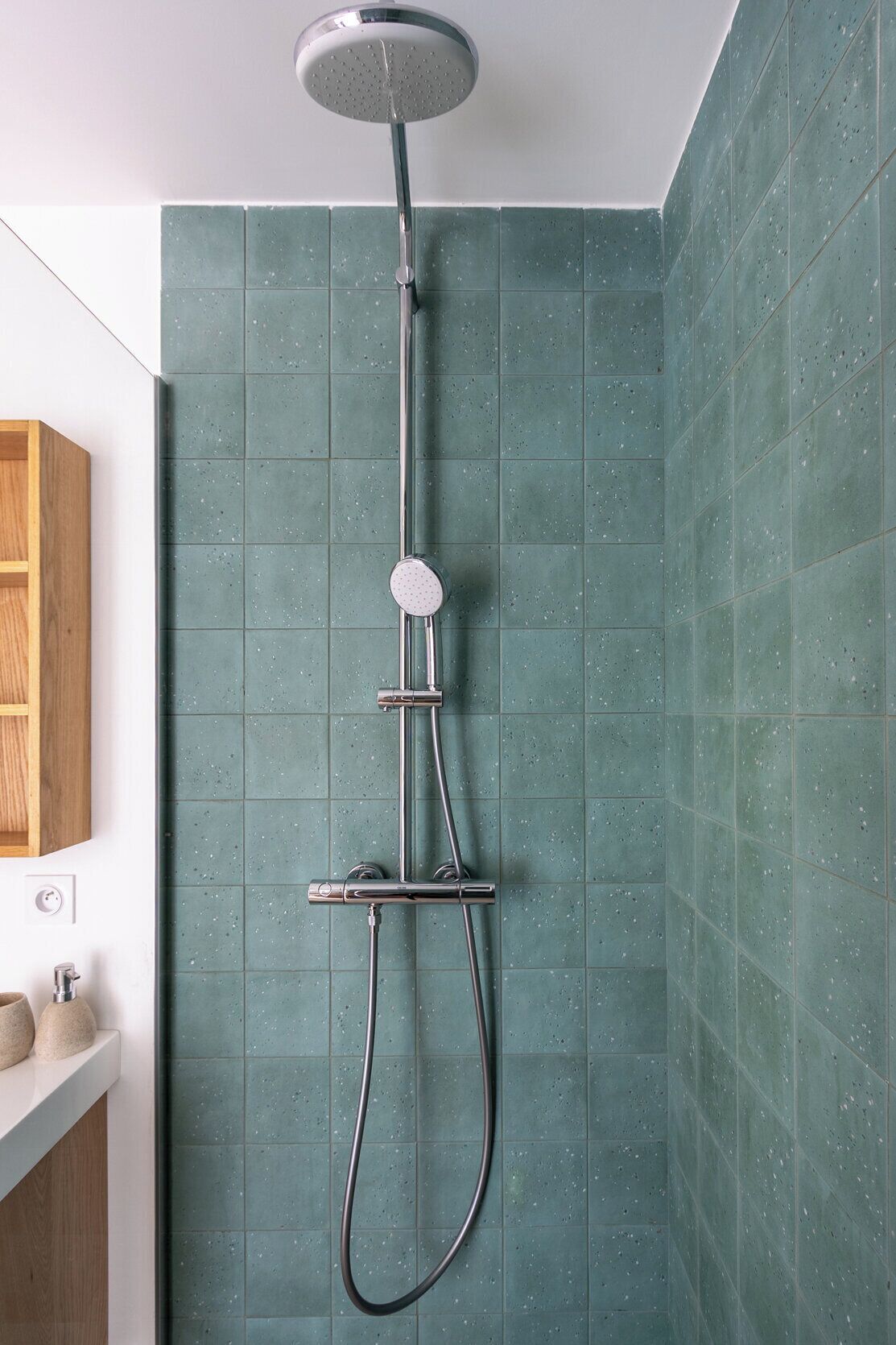 A shower with a handheld showerhead and a handheld faucet, mounted on a wall with speckled tiles.