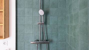 A shower with a handheld showerhead and a handheld faucet, mounted on a wall with speckled tiles.