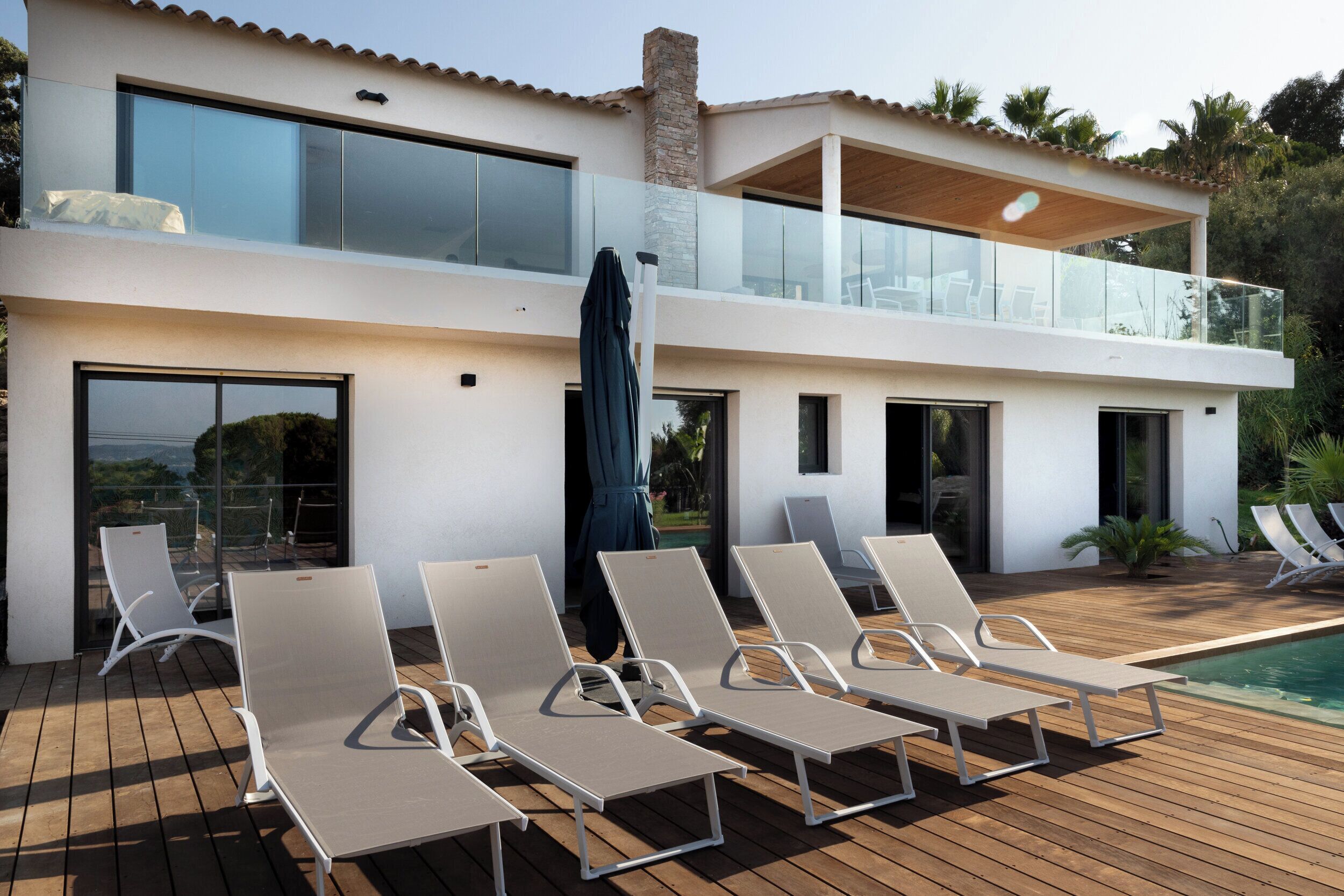 A modern two-story house with a pool, sun loungers, and a glass balcony.