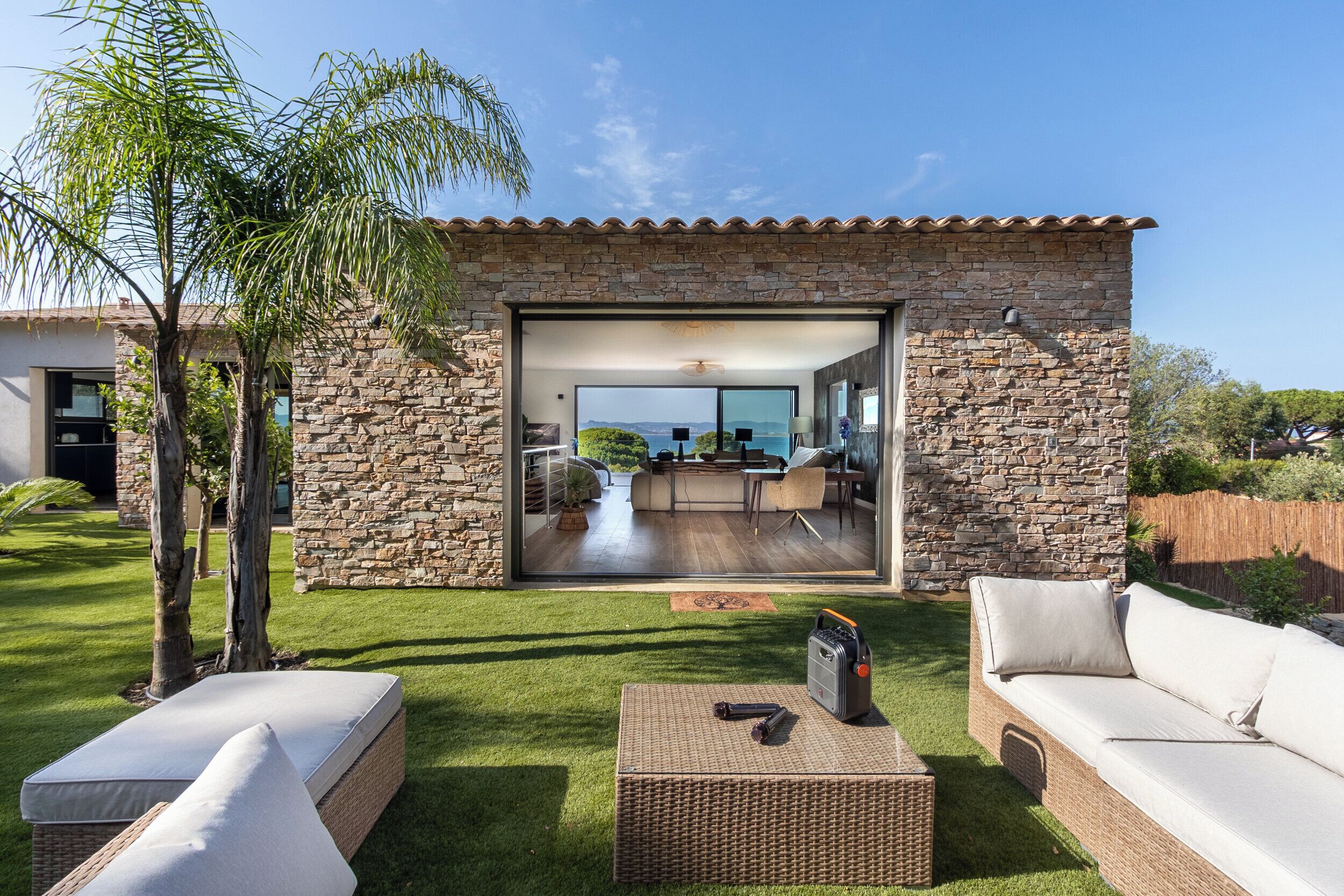 A modern house with a stone exterior, a glass door leading to a living area with a view, and outdoor furniture.