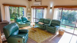 A living room with green leather sofas, a glass coffee table, and a yellow patterned rug.