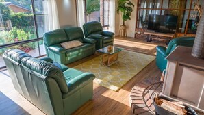 A living room with green sofas, a glass coffee table, a TV, and a fireplace.