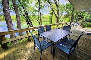 A wooden deck with a table and chairs, overlooking a body of water and surrounded by trees. - Private Arcade Room | Family Home Near Waterparks (Wisconsin Dells)