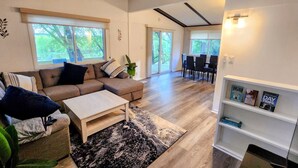 A modern living room with a sectional sofa, a coffee table, and a dining area with chairs and a table. - Arcade Room + Fire Pit + Creek Views | Near Waterparks (Wisconsin Dells)