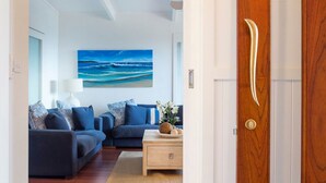 A modern living room with a large ocean-themed painting on the wall, a blue sofa set, and a wooden coffee table with decorative items.