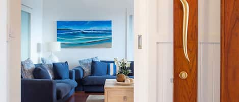 A modern living room with a large ocean-themed painting on the wall, a blue sofa set, and a wooden coffee table with decorative items.