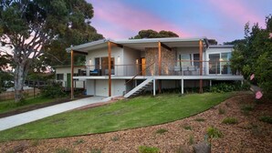 A modern two-story house with a covered patio, a stone facade, and a well-maintained lawn.