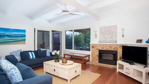 A modern living room with a sofa, coffee table, TV, fireplace, and large windows.