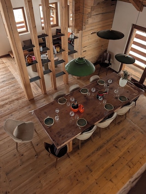 Uma mesa de jantar de madeira com cadeiras, uma luminária pendente verde e um vaso com flores.