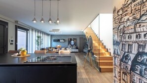 A modern kitchen with a central island, a dining area with a sofa and table, and a staircase with a cityscape mural. - Detached House with Landscape Views and Charm in the Heart of the Basque Country (MARKAIDA)