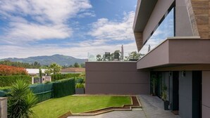 A modern building with a flat roof, a large glass window, and a well-maintained garden with a lawn and a small pond. - Detached House with Landscape Views and Charm in the Heart of the Basque Country (MARKAIDA)