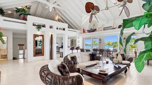 A spacious living area with high ceilings, a large dining table, wicker furniture, and a view of the outdoors. - Villa 3: islandpropertiesonline: 5-bedroom villa infinity pool & terrace (Maho)