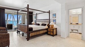 A four-poster bed with a wooden frame, a bedside table with a lamp, and a view of the sea through large windows. - Villa 3: islandpropertiesonline: 5-bedroom villa infinity pool & terrace (Maho)