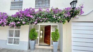 En bygningseingang med en trædør, en balkon med hvide gelændere og en væg dækket af blomster.