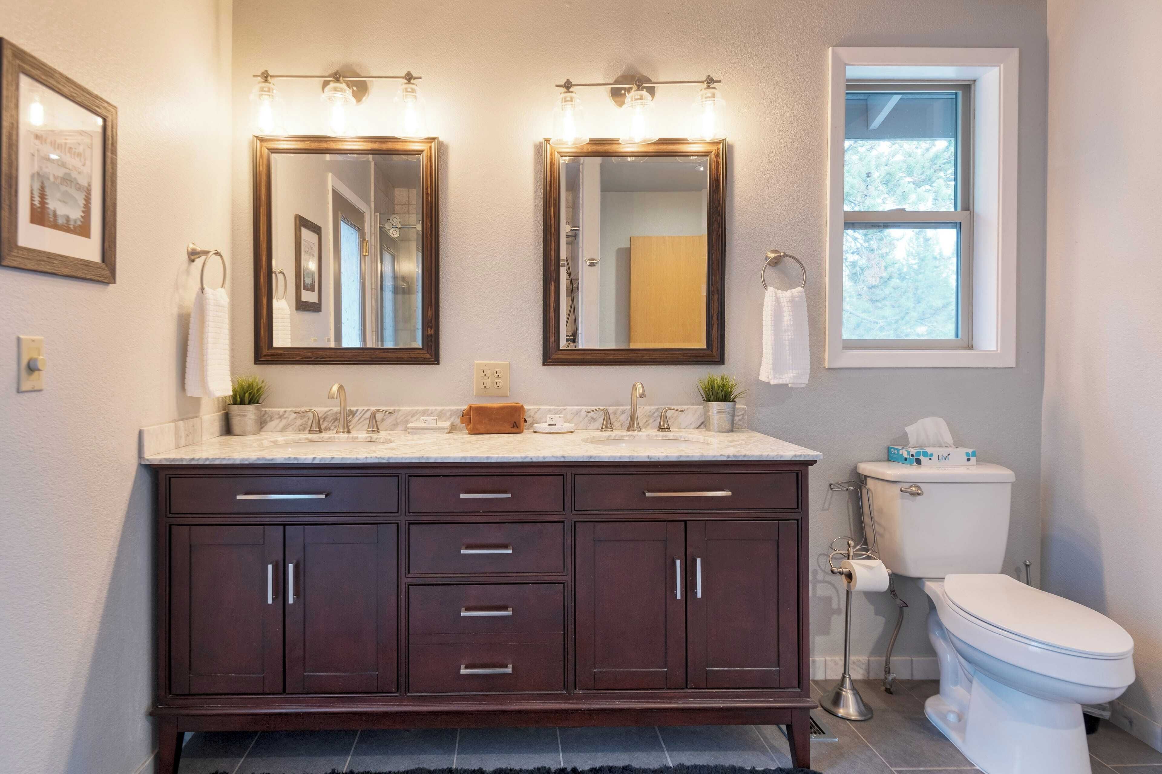 A bathroom with a dark wood vanity, two mirrors, a toilet, and a window.