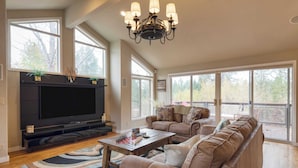 A spacious living room with a large flat-screen TV, comfortable seating, and large windows offering a view of the outdoors. - Private Boat Ramp Access Hot Tub, Fire Pit, Deck River Meadows by Avantstay (Bend)