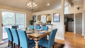 A dining room with a wooden table and blue upholstered chairs, a chandelier, and a kitchen in the background. - Private Boat Ramp Access Hot Tub, Fire Pit, Deck River Meadows by Avantstay (Bend)