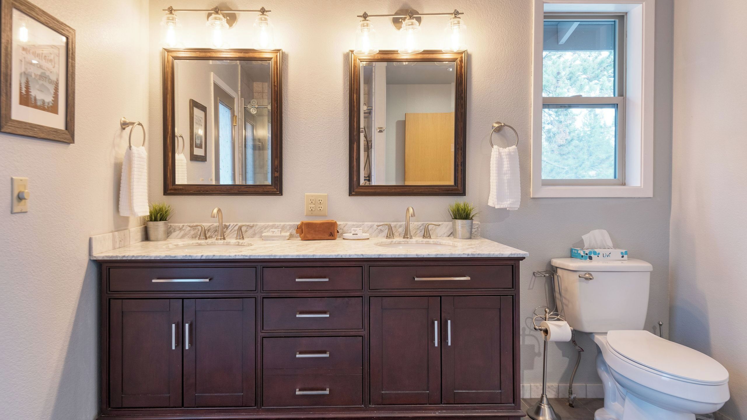 A bathroom with a vanity, two mirrors, a toilet, and a window.