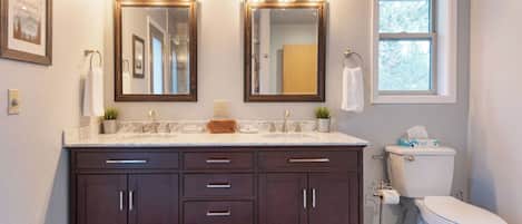 A bathroom with a vanity, two mirrors, a toilet, and a window.