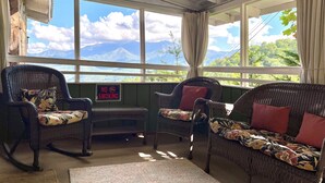 A cozy room with wicker furniture, a 'NO SMOKING' sign, and a view of mountains through large windows. - Beautiful Cabin in Chalet Village. Hot Tub, 3 Decks, Stunning Mountain Views  (Gatlinburg)