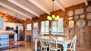 A wooden interior with a dining table, chairs, a chandelier, and kitchen appliances. - Beautiful Cabin in Chalet Village. Hot Tub, 3 Decks, Stunning Mountain Views  (Gatlinburg)