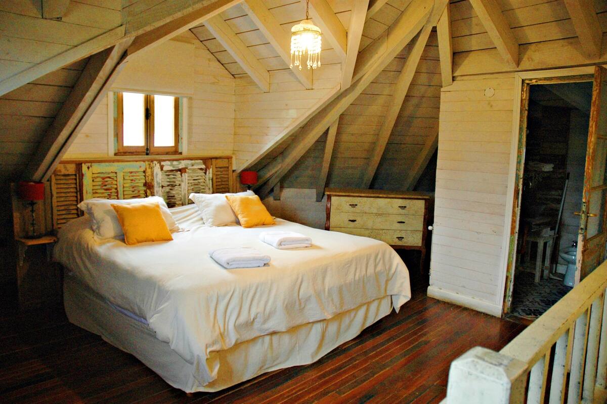 A bedroom with a large bed, wooden beams, a chandelier, and a wooden door.