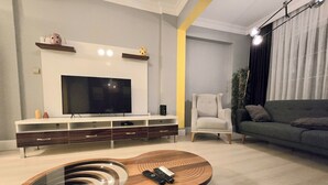 Uma sala de estar moderna com televisão de tela plana, uma mesa de centro em formato de guitarra, sofá cinza e design minimalista.