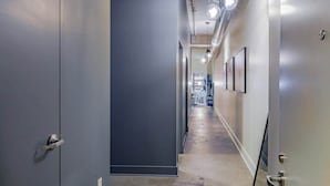 A hallway with grey walls, a concrete floor, and a ceiling with exposed ductwork and hanging lights. - Historic 2BR Loft: Private Terrace & Free UFC Gym (Pittsburgh)