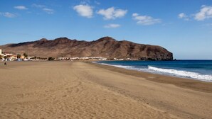 A wide sandy beach with a mountain in the background. - Mar&mar apartment with solarium and swimming pool. (Gran Tarajal)