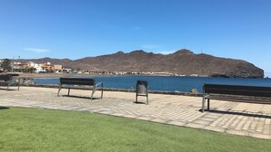A paved outdoor area with two benches facing a body of water and a mountain in the background. - Mar&mar apartment with solarium and swimming pool. (Gran Tarajal)