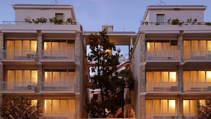 Un edificio moderno con varios balcones y ventanas, que presenta una escalera central y abundante vegetación.