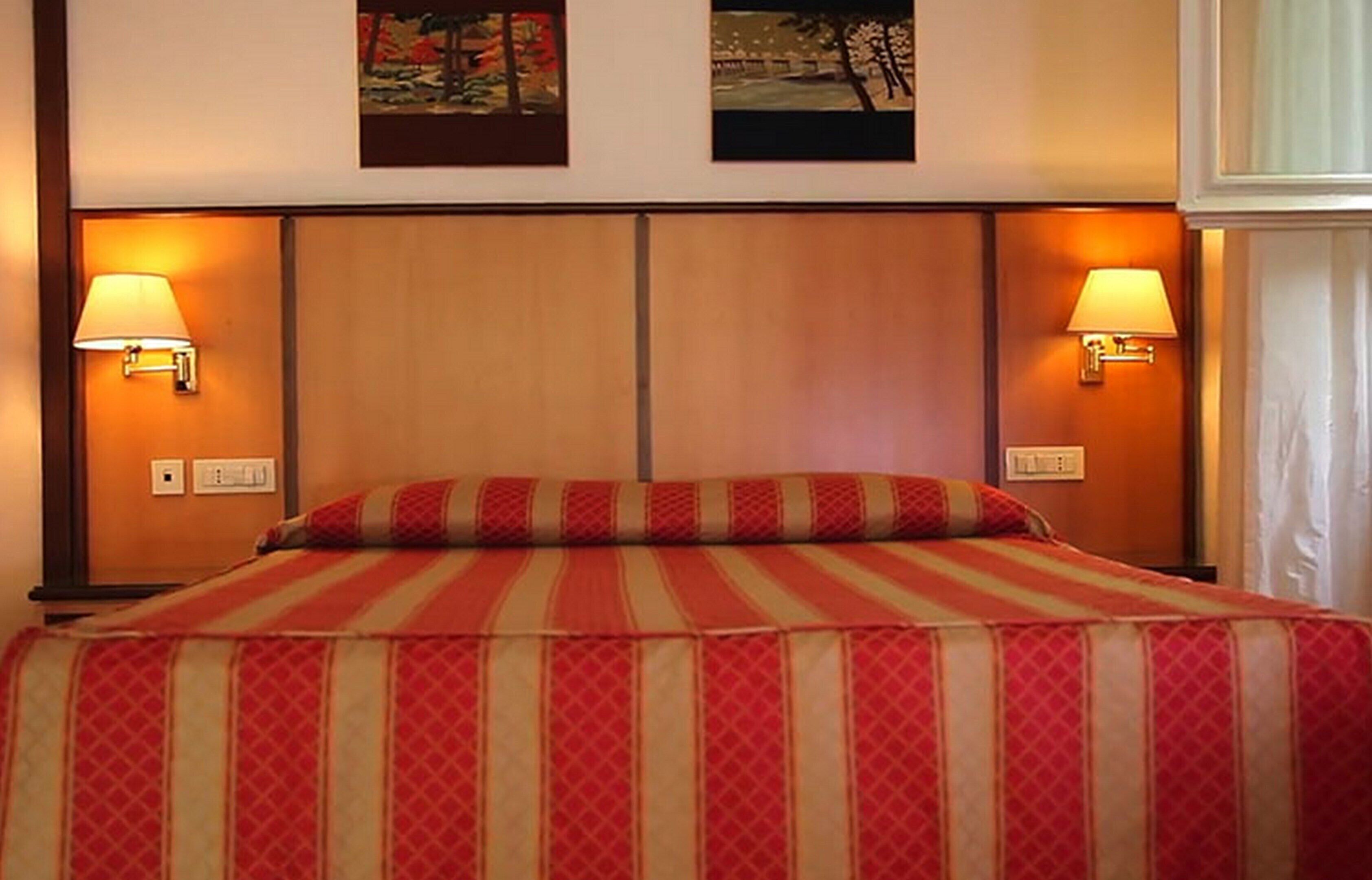 Une chambre d’hôtel avec un grand lit, deux lampes fixées au mur et deux tableaux encadrés au-dessus du lit.