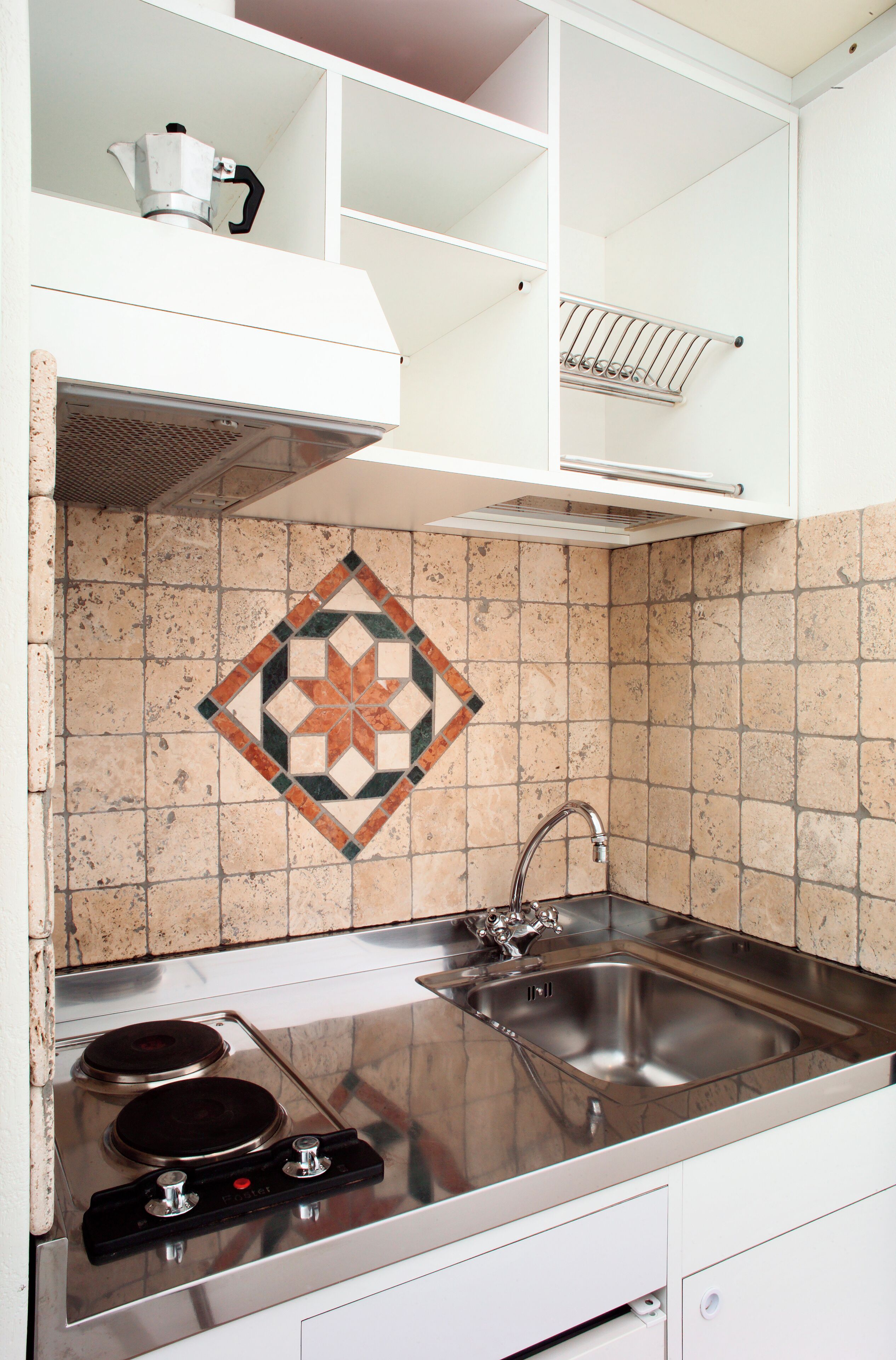 Eine Küche mit Spüle aus Edelstahl, einem Herd und einer Spritzschutzwand mit geometrischem Fliesendesign.