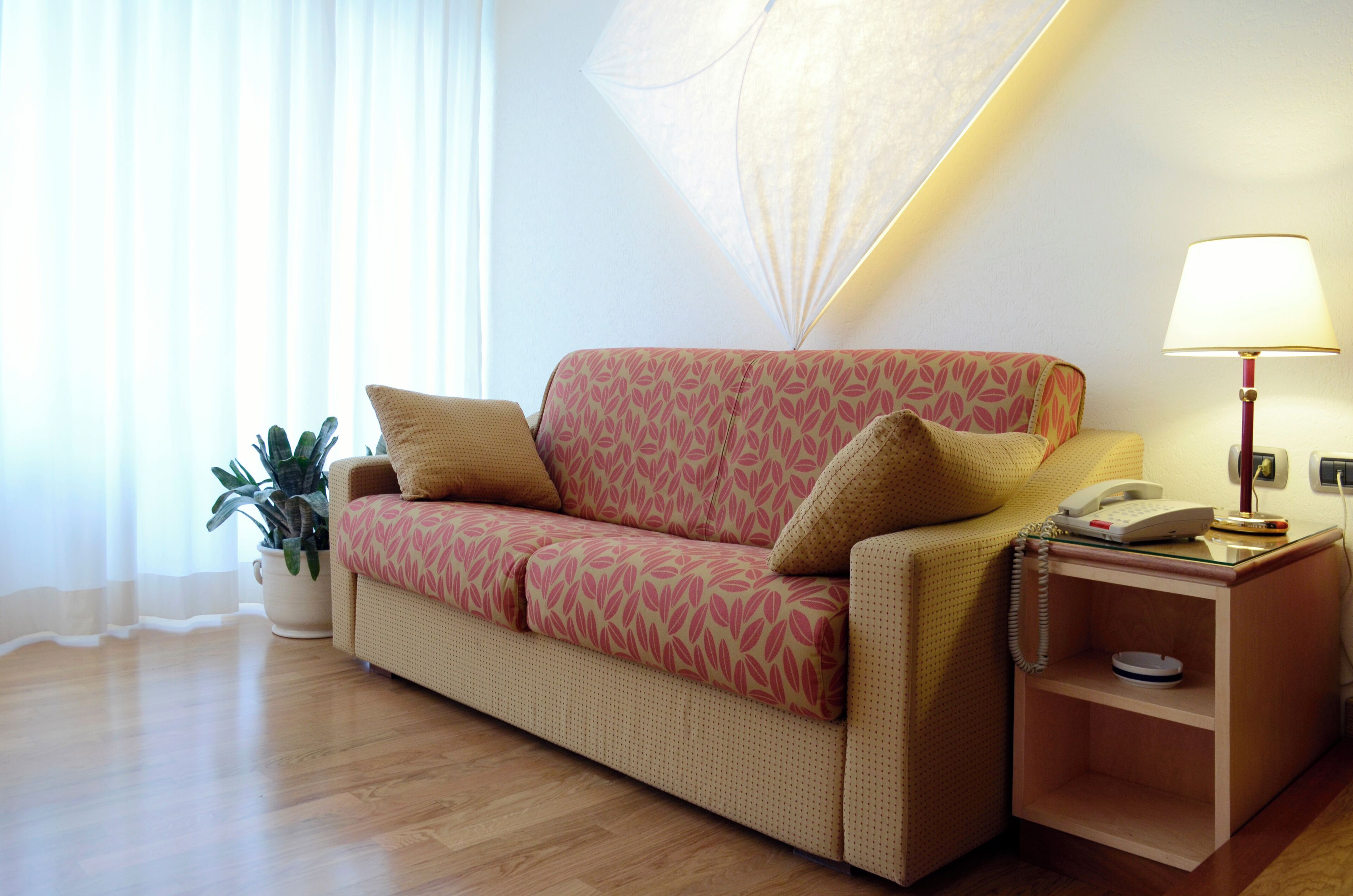 Una habitación con sofá, lámpara, teléfono y planta.