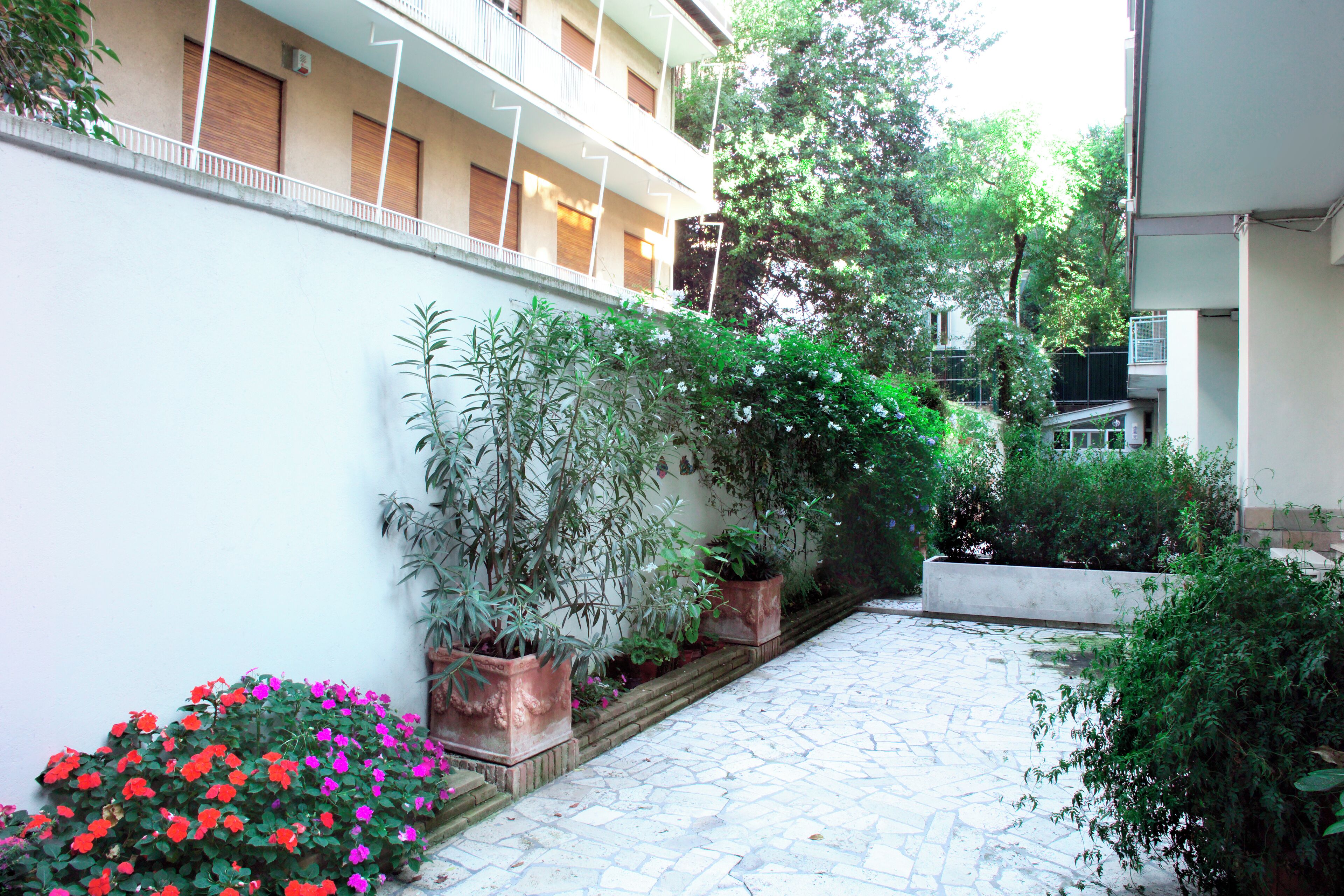 A courtyard with a stone pathway, potted plants, and a building with balconies.