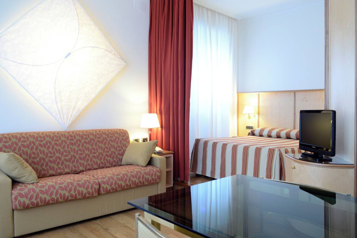 A hotel room with a sofa, a bed with striped bedding, a television, and a lamp.