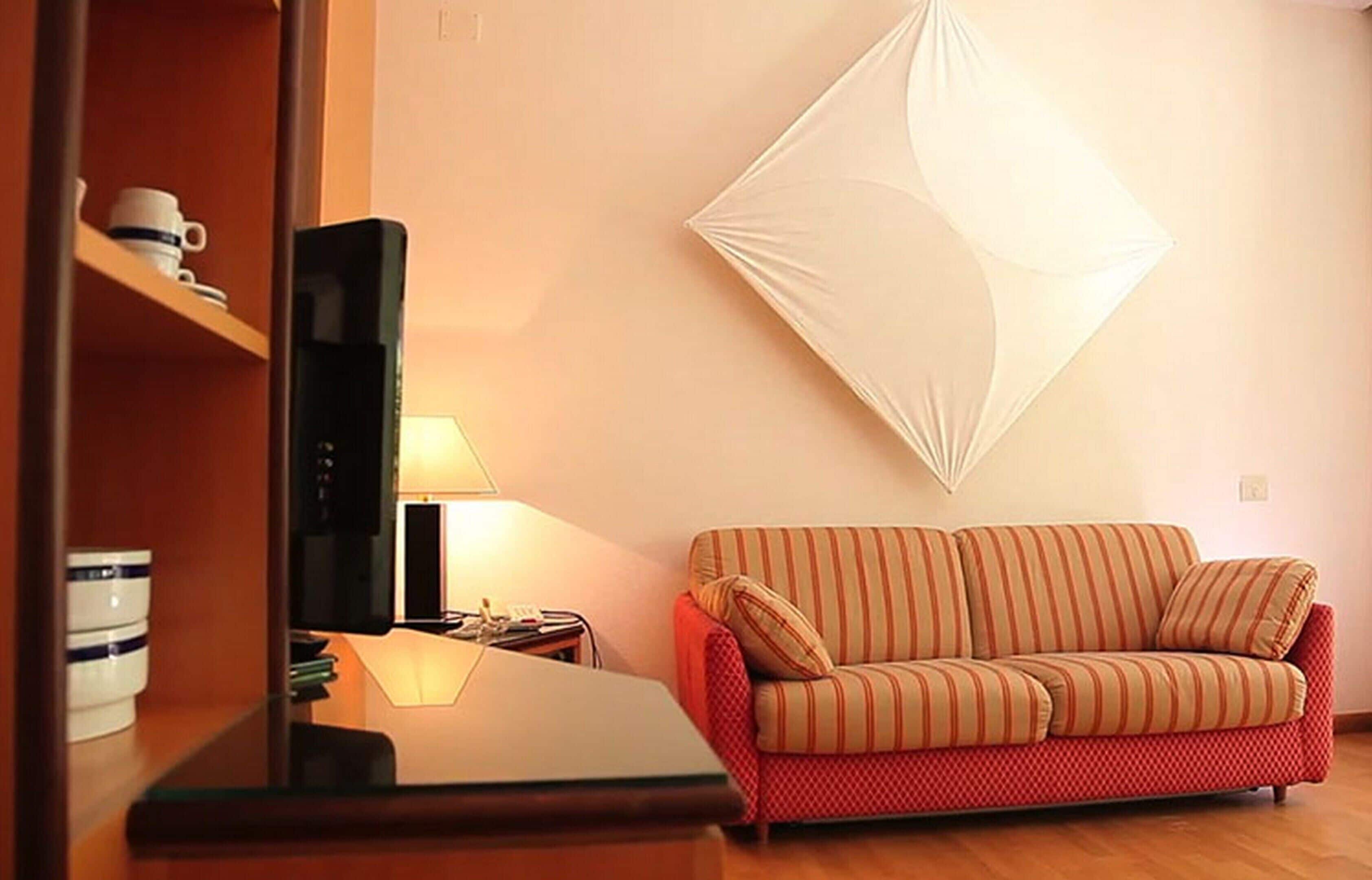 A living room with a red sofa, a television, a lamp, and a wall-mounted decorative piece.