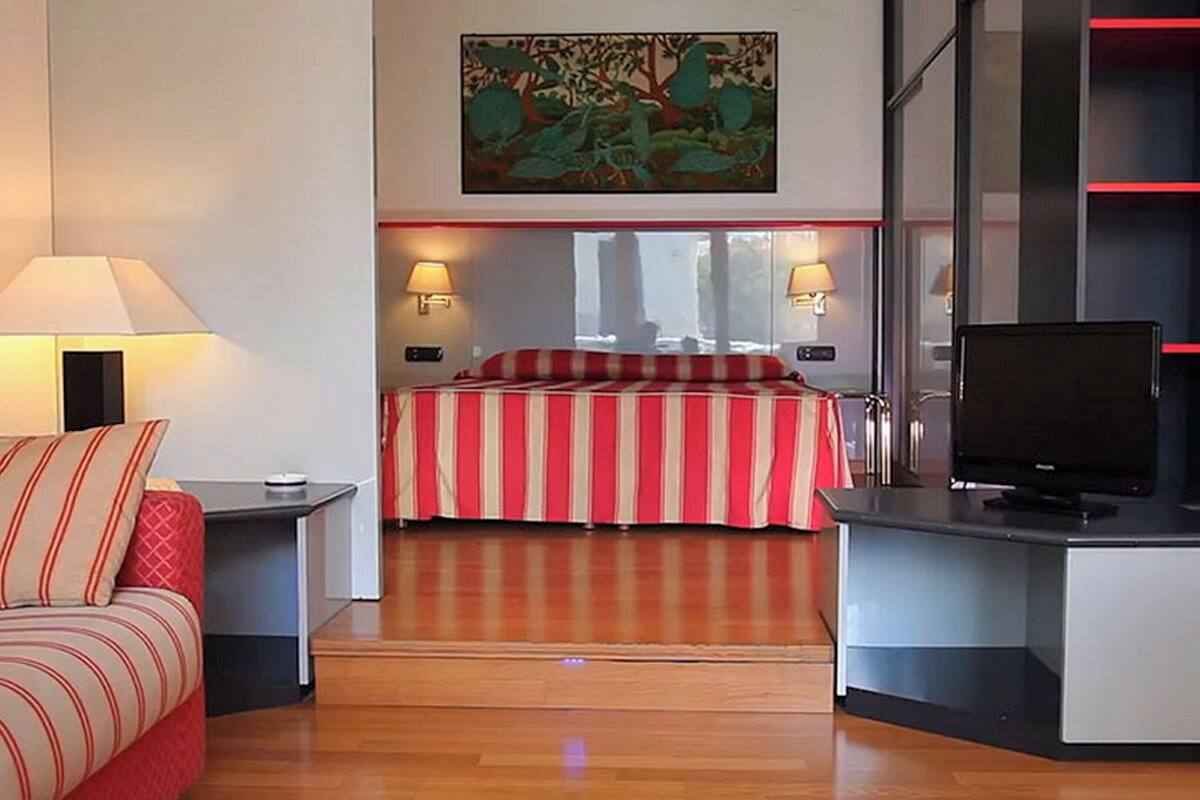 A hotel room with a bed, a desk with a TV, and a painting on the wall.