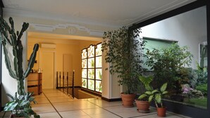 Un pasillo espacioso con suelo de baldosas, plantas en macetas y vistas de un jardín a través de una ventana.