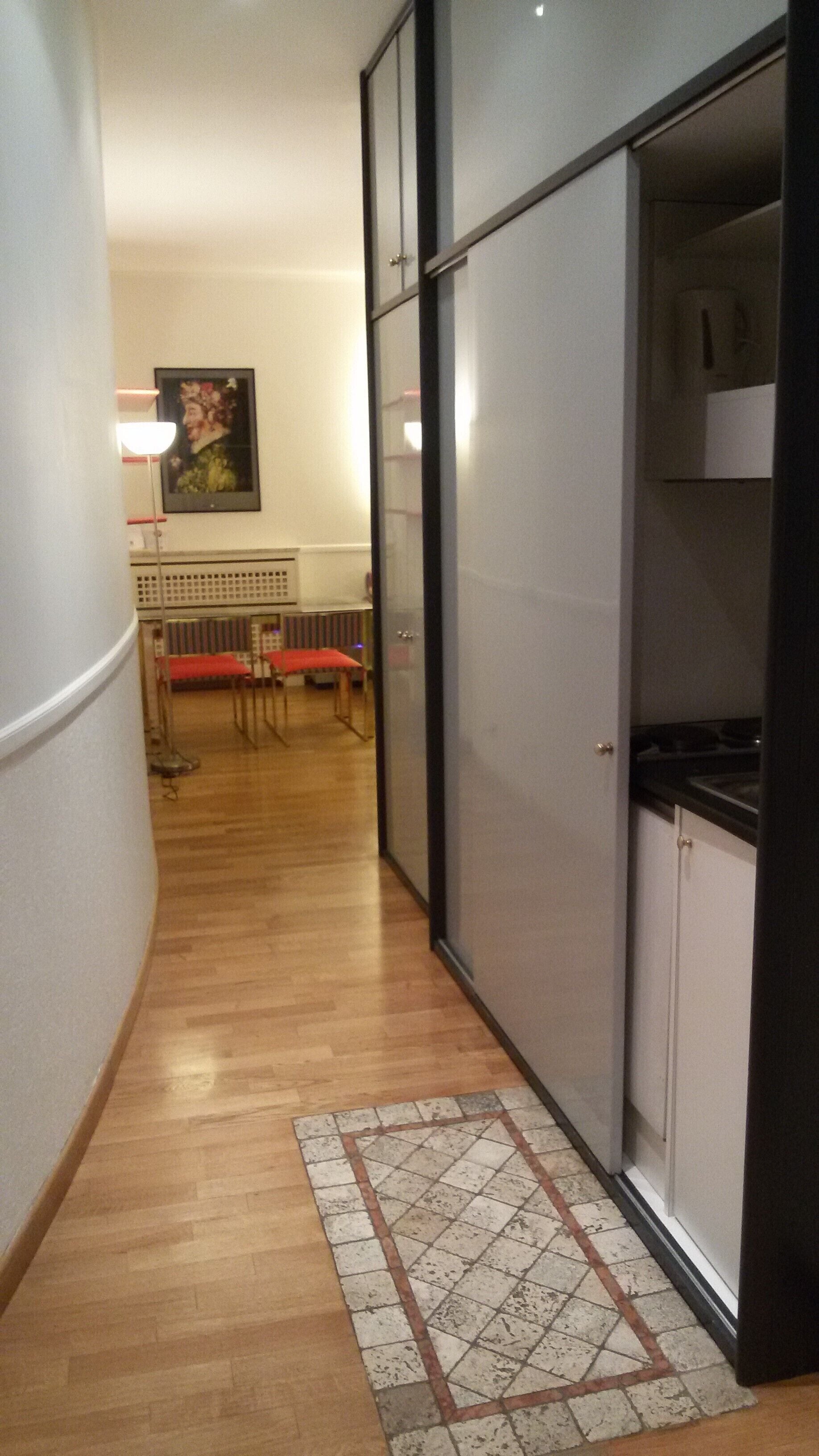 En smal hall med trägolv, en kakelmatta vid ingången och en matplats med ett bord och stolar i bakgrunden.
