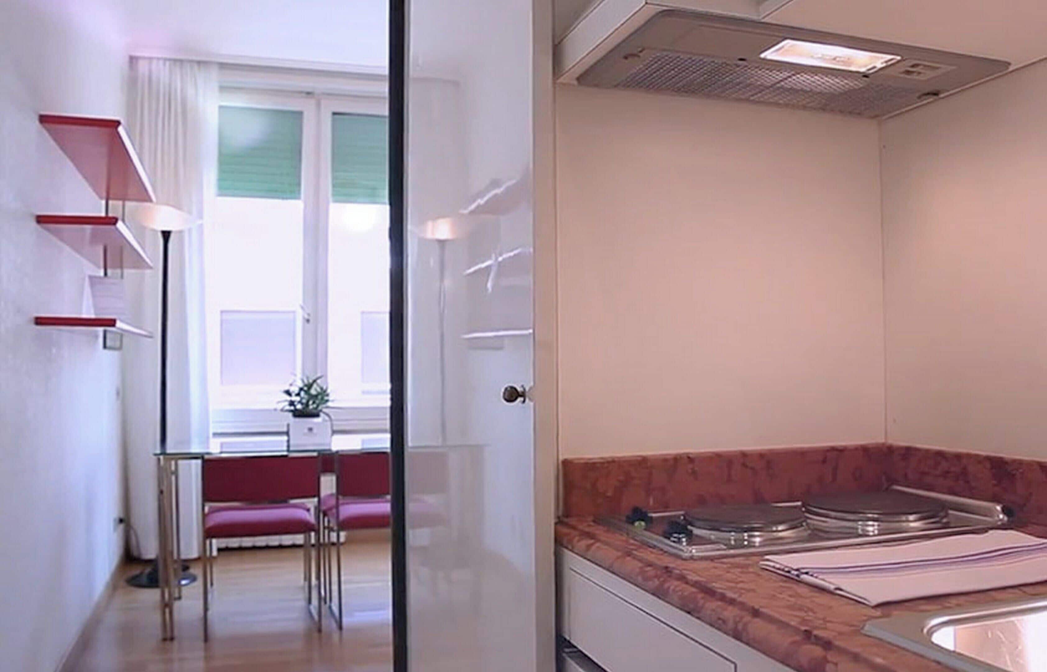 A compact kitchen with a countertop, sink, and a window with blinds.