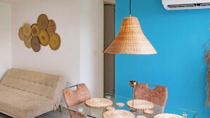Ein modernes Wohnzimmer mit einem Glastisch, gepolsterten Stühlen, einer Hängeleuchte und einem Wandbild.
