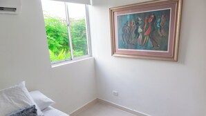Ein Schlafzimmer mit Bett, einem Fenster mit Blick auf Grünflächen und einem Bild an der Wand.