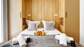 Una habitación compacta con una cama, dos almohadas, una bandeja con productos de desayuno y una caja de bienvenida.
