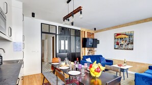 Una sala de estar moderna con comedor, un sofá azul y un televisor montado en la pared.