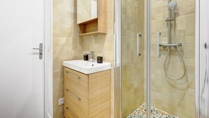 Un baño moderno con cabina de ducha de vidrio, tocador de madera con lavabo blanco y un armario con espejo sobre el lavabo.