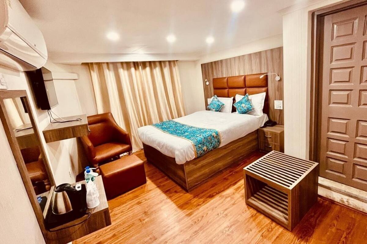 A hotel room with a wooden bed, a bedside table, a chair, a small desk, and a wardrobe.