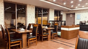 Un restaurante con mesas y sillas de madera, un mostrador de recepción y papel tapiz estampado.