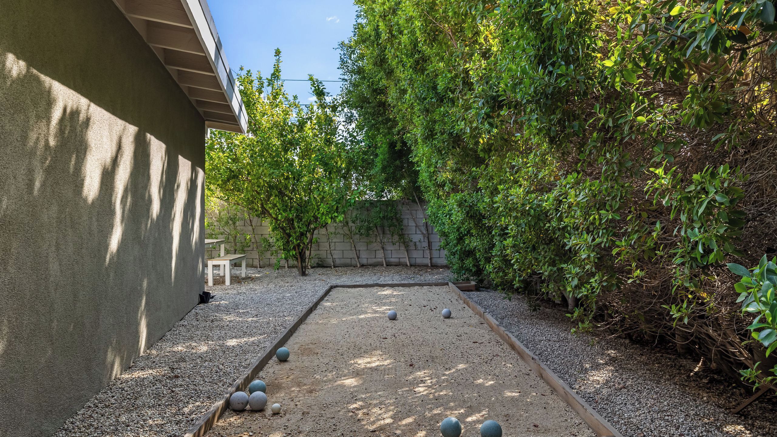 A courtyard with a gravel area, a white bench, and a wall with climbing plants.