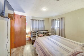 Et soveværelse med seng, en trædør, et lille bord med lampe og et vindue med gardiner.